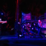 Dan Donohue as Macbeth, standing in front of the ensemble cast with dark lighting
